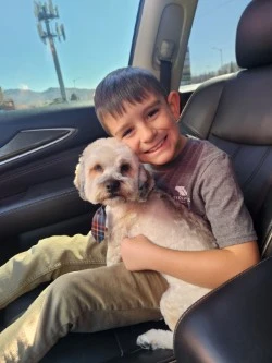 A young boy named Bentley, sitting in a car and holding a small white dog while smiling at the camera A young boy named Bentley, sitting in a car and holding a small white dog while smiling at the camera