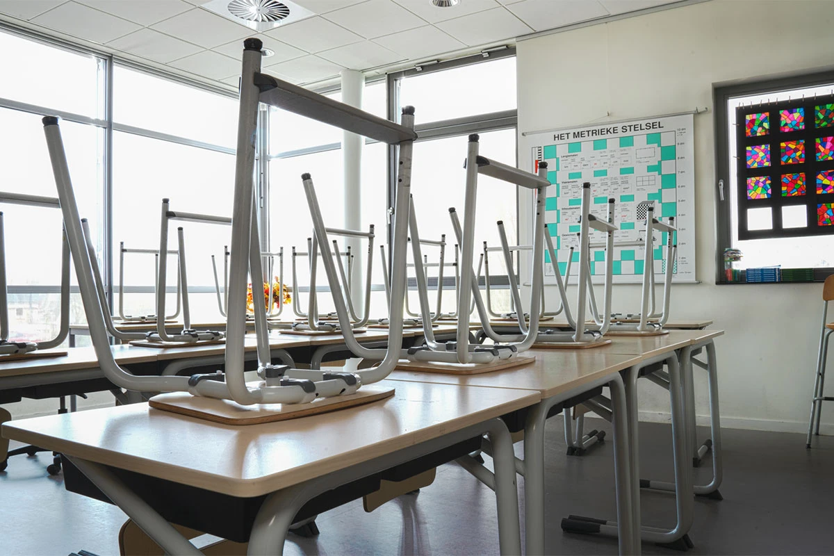 An empty classroom with stairs stacked on their desks as the sun shines through the window